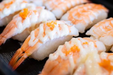 Kremalı mayonez ve turuncu balık yumurtası ile kaplanmış Ebi karidesli nigiri. Lezzetli Japon deniz ürünleri aperatifleri siyah tabakta servis edilir, yakın plan..