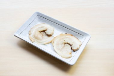 Kavrulmuş Japon chashu domuz eti dilimleri beyaz bir seramik tabakta servis edilir ahşap arka planda, popüler bir ramen üstü..