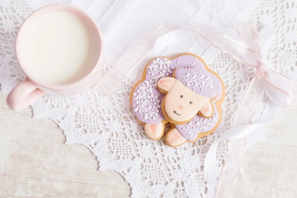 Lavender gingerbread sheep with cup of milk on lace tablecloth. — Stock Photo, Image