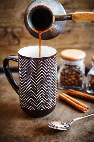 Kaffee fließt aus einem Kupferkessel in einen braunen Becher — Stockfoto
