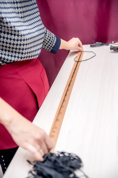 An employee of the Studio measures the tape. Seamstress at the cutting table in an apron. An employee in the form measures using a ruler.