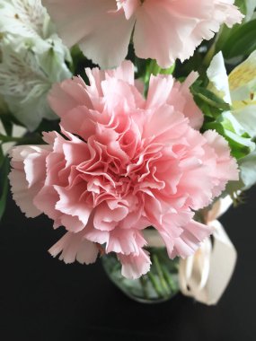 Diğer çiçeklerle çevrili şeffaf bir vazoda pembe karanfil.