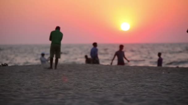 Ludzie odpoczynek na plaży o zachodzie słońca — Wideo stockowe