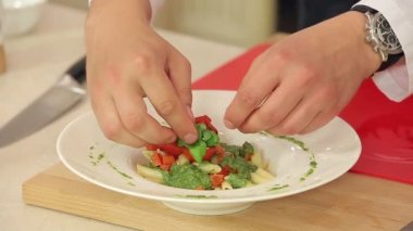 Taze fesleğen ve ezilmiş biber yeşil Pesto ve Fried ile makarna koyarak Şef bir tabak içinde kırmızı kiraz domates