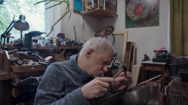 Tekerlekli sandalyede usta bir zanaatkar atölyesinde çalışıyor. Japon kılıcının ucuna çekiç ve keskiyle hormon resmi işliyor.