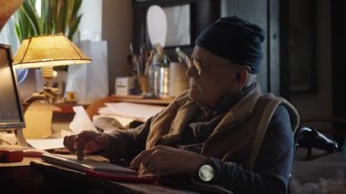 Kronik engelli yaşlı yetişkin tekerlekli sandalyede oturan bilgisayarla çalışıyor.