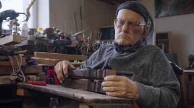Tekerlekli sandalyedeki yaşlı erkek usta atölyesinde mobilyaları restore ediyor.