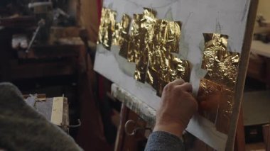 Tekerlekli sandalyedeki kıdemli sanatçı tuvaldeki yağlı boyaya altın sürüyor.