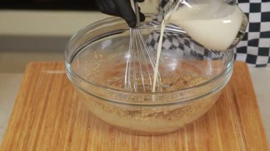 Şef kahverengi şekerle sütü karıştırıyor cam kasede hamur çırpıyor.