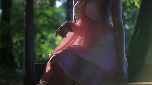 Dívka v růžových šatech sedí na lavičce za slunného letního dne — Stock video