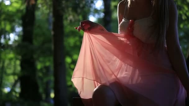 Chica en un vestido rosa sentada en el banco en un día soleado de verano — Vídeo de stock