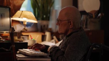 Kronik engelli yaşlı yetişkin tekerlekli sandalyede oturan bilgisayarla çalışıyor.