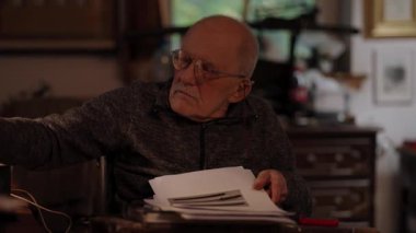 Kronik engelli yaşlı yetişkin tekerlekli sandalyede oturan masaüstü bilgisayarının evraklarıyla çalışıyor.