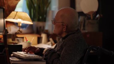 Kronik engelli yaşlı yetişkin tekerlekli sandalyede oturan bilgisayarla çalışıyor.