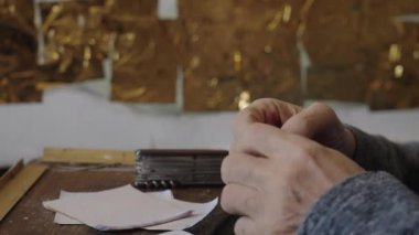 Tekerlekli sandalyedeki kıdemli sanatçı tuvaldeki yağlı boyaya altın sürüyor.