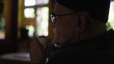 Tekerlekli sandalyede oturan yaşlı bir adam evin oturma odasında televizyon izliyor.