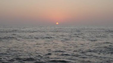 Gün batımında kayalık bir plaja vuran temiz deniz dalgaları.