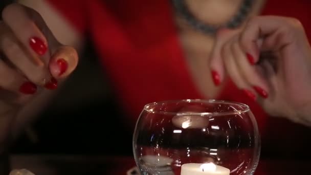 Όμορφη μελαχρινή με κόκκινο φόρεμα που παίζει με ένα κερί και τήξης παγάκια στο καθρέφτη τραπέζι — Αρχείο Βίντεο