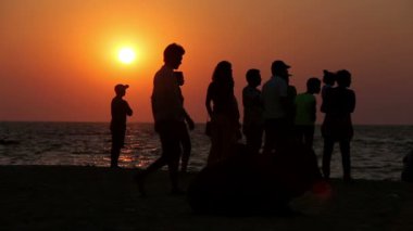 Gün batımında sahilde oturan insanlar