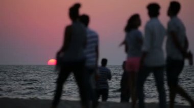 Gün batımında sahilde oturan insanlar