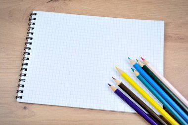 Ahşap bir masanın üzerinde renkli kalemlerle dolu boş bir defter.