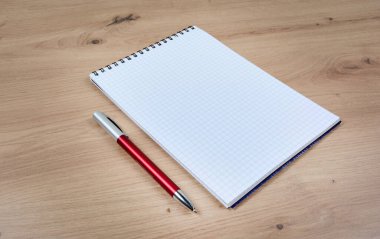 Ahşap bir masanın üzerinde kırmızı kalemle boş bir defter