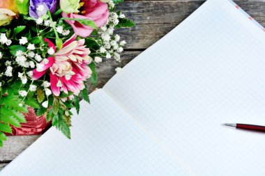 Kalem ve çiçeklerle dolu boş bir defter eski bir ahşap masada. Üst görünüm