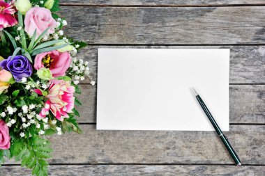 Boş kağıt kalem ve çiçekler eski bir ahşap masada.