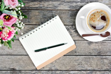 Kalem, kahve fincanı ve renkli çiçeklerle dolu boş bir defter.