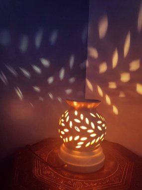 Seramik lamba delikleri benekli ışık desenleri ve duvarda gölgeler bırakıyor. Güzel sanat. Karanlık arka plan. Romantik ruh hali.