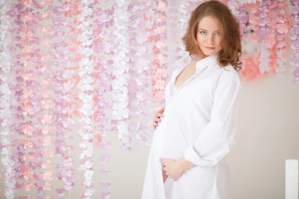 Mujer embarazada de color rosa sobre un fondo de flores —  Fotos de Stock
