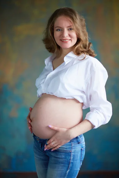 Беременная женщина в джинсах в студии — стоковое фото