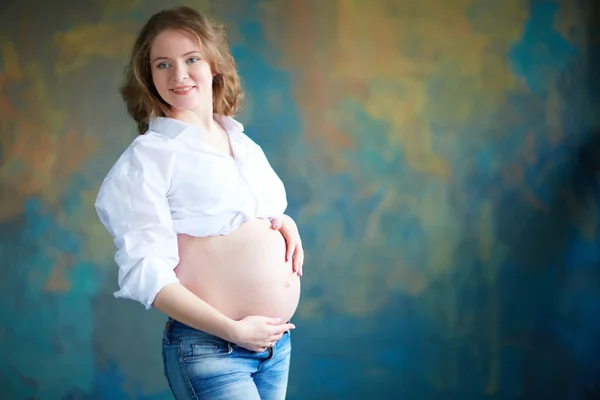 Těhotná žena v džínách ve studiu — Stock fotografie