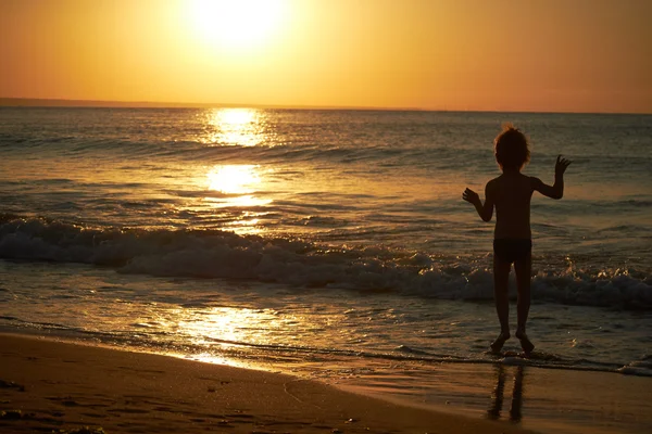 Мальчик играет на пляже на закате — стоковое фото