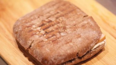 Closeup of persons hand cutting freshly baked sandwich with knife 