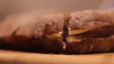 Closeup of persons hand cutting freshly baked sandwich with knife 