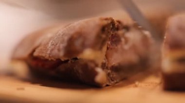 Closeup of persons hand cutting freshly baked sandwich with knife 