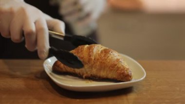 Closeup of persons hand putting freshly baked croissant on white plate 