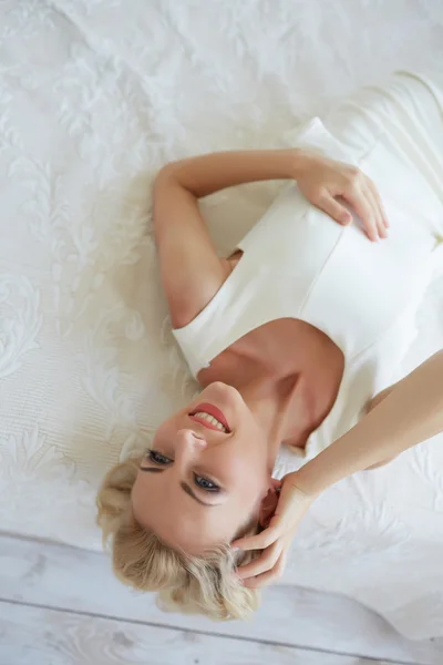 Kvinnan i vit klänning ligger på sängen — Stockfoto