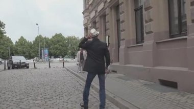 Siyah takım elbiseli erkek model ve beyaz şapka video için poz veriyor