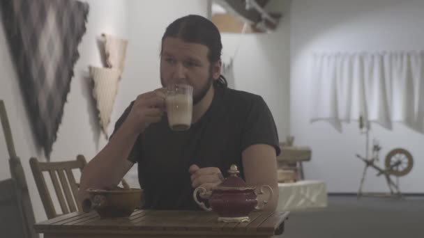 Uzun siyah saçlı ve sakallı sakin bir adam kafede kahve içer. — Stok video