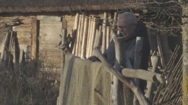 Gözlüklü ve ceketli adam eski çitlerdeki balık ağını çözüyor.