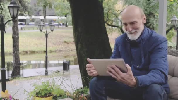 Stilvoller älterer Mann lächelt beim Blick auf Tablet-Bildschirm im Café — Stockvideo