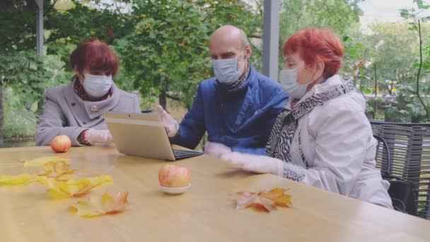 Emeryci przyjaciele w maskach medycznych odpocząć w kawiarni parku — Wideo stockowe