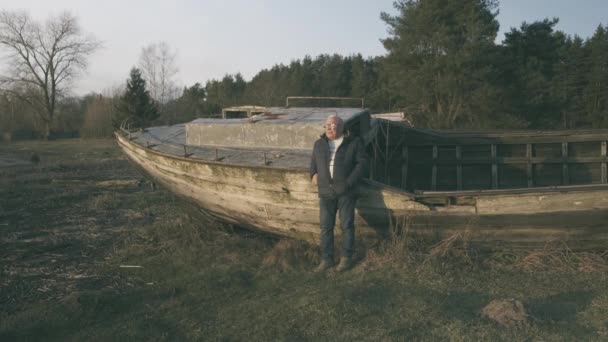 Starszy człowiek stoi w pobliżu zniszczony starożytnych dużych drewnianych łodzi — Wideo stockowe