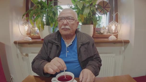 Gepensioneerde man met een bril roert suiker in een kopje fruitthee — Stockvideo