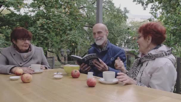 Emeryt trzyma książkę o rozmowie z eleganckimi kobietami — Wideo stockowe