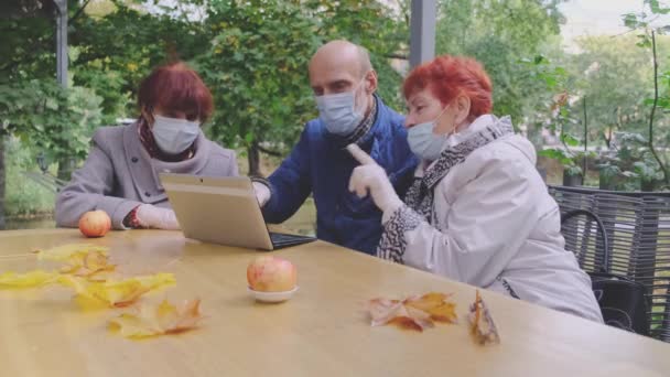 Amis retraités dans des masques de protection reposent dans un café de parc ouvert — Video