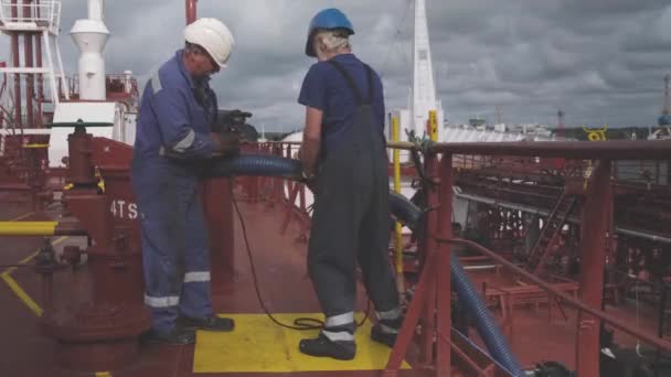 Tanker sailors give large black hosepipes through handrails — Stock Video