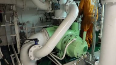 Vatman tanker makine dairesinde büyük bir pompayla çalışıyor.